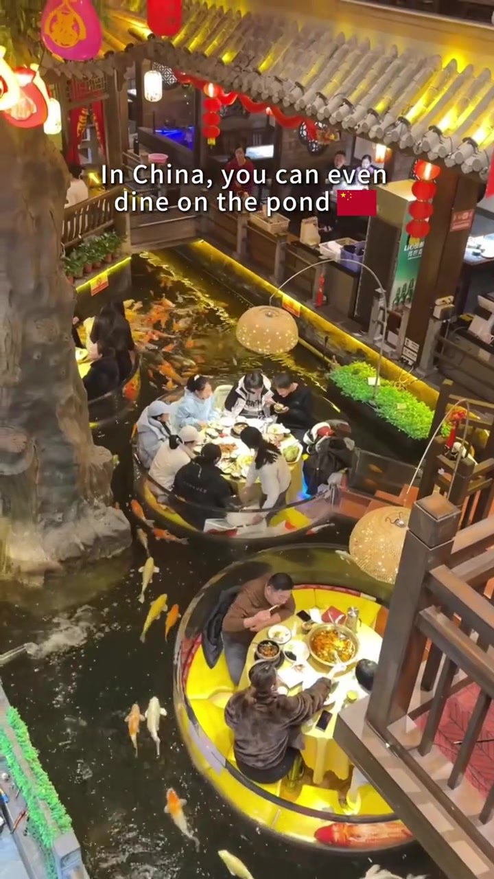 Two illuminated circular dining booths viewed above a narrow indoor koi pond