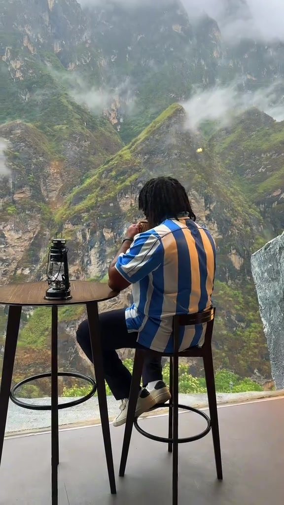 Traveller drinking coffee while facing green mountains and low cloud