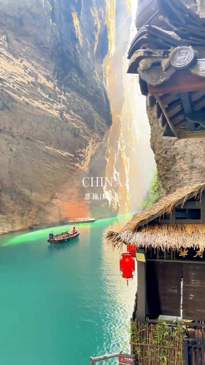 A small boat beneath towering cliffs beside traditional-style buildings