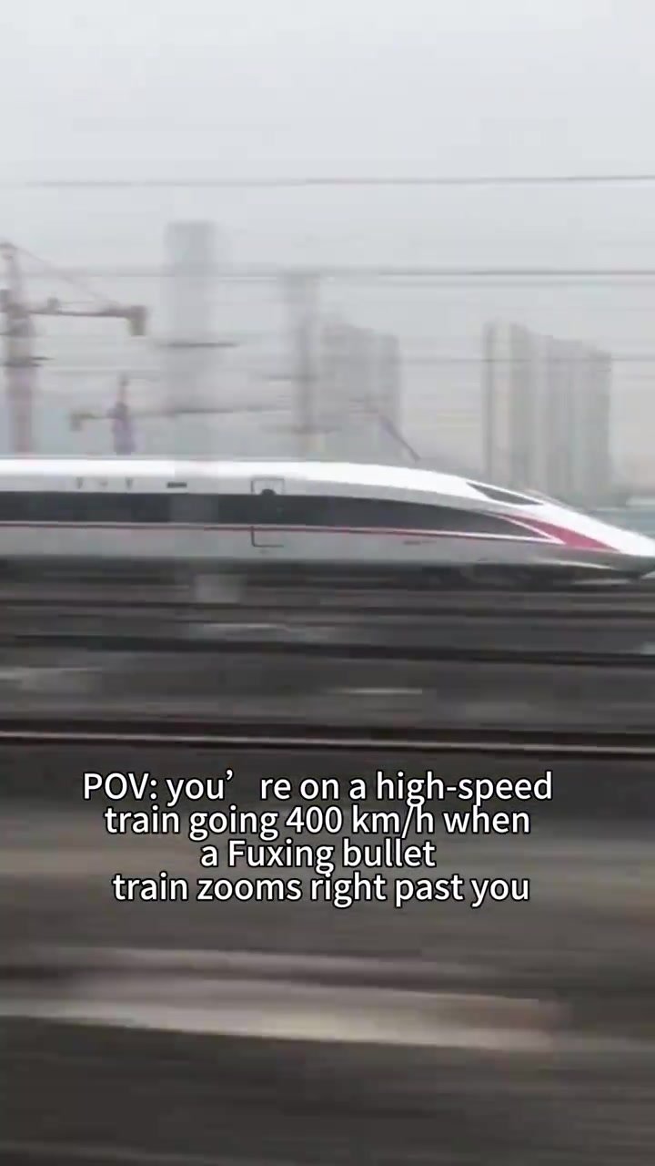 Fuxing high-speed train racing past urban buildings and railway infrastructure
